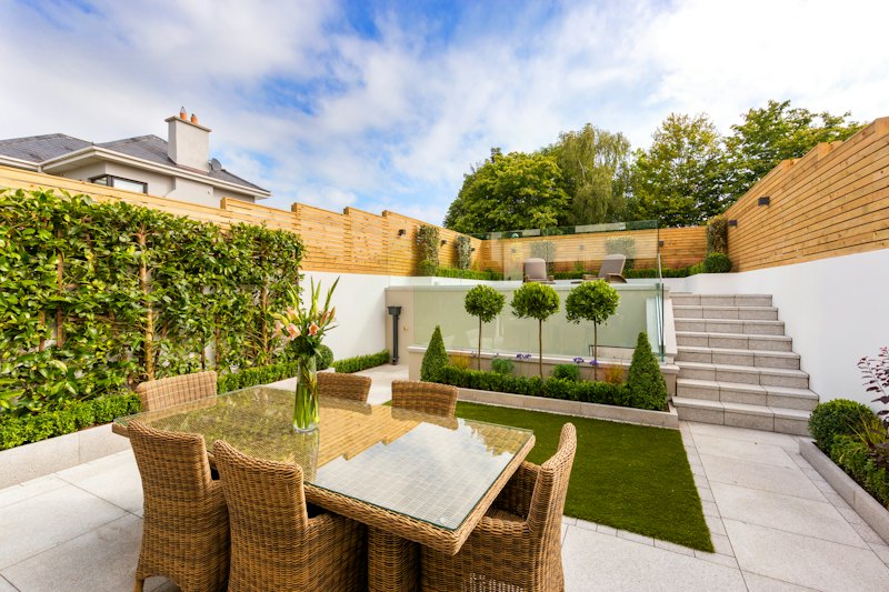 Terrasse dallée et table de jardin entourée de haies